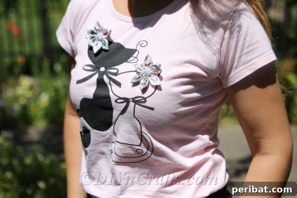 A pair of handmade fabric flowers, featuring textured petals and shimmering centers, thoughtfully pinned to a simple t-shirt.