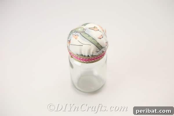 Clever Pincushion Jar Sewing Caddy 15 A newly crafted pincushion jar, featuring a cheerful fabric top and a decorative ribbon, proudly displayed on a surface.