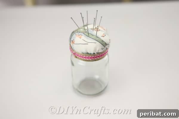 Clever Pincushion Jar Sewing Caddy 16 Close-up of a completed pincushion jar with various colorful pins neatly stuck into its soft fabric top, sitting on a wooden table.
