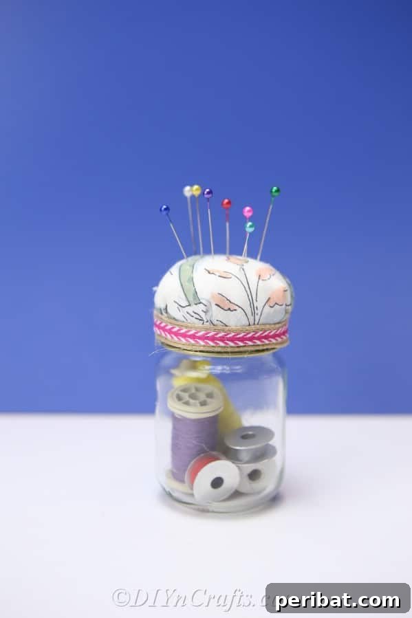 Clever Pincushion Jar Sewing Caddy 18 A stylish pincushion jar, complete with a patterned fabric top and ribbon, set against a calming blue backdrop, highlighting its handcrafted beauty.