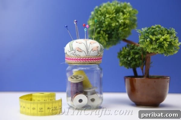 Clever Pincushion Jar Sewing Caddy 21 A pincushion jar, a small green plant, and a yellow tape measure neatly arranged on a blue surface, showcasing a peaceful crafting setup.