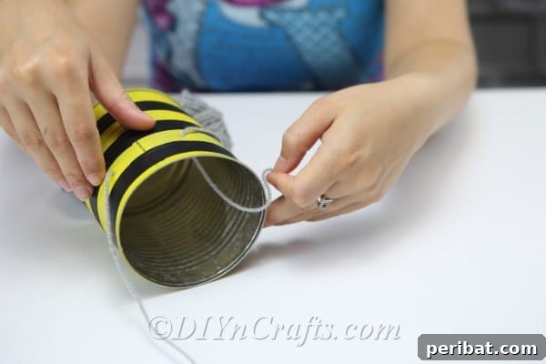 A picture showing a woman threading twine through holes to create legs on bee craft