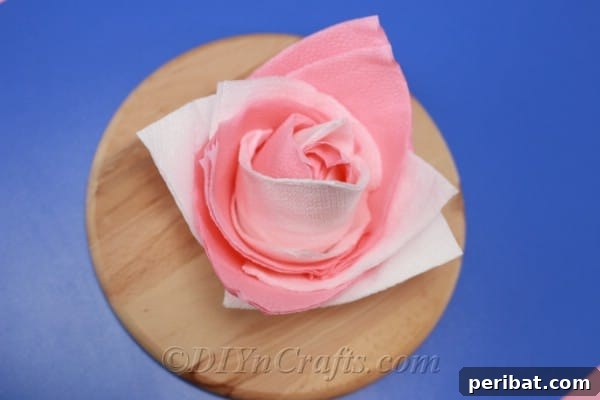 Overhead image of a paper napkin flower sitting on a wooden board on a blue surface created from the how to fold napkins tutorial