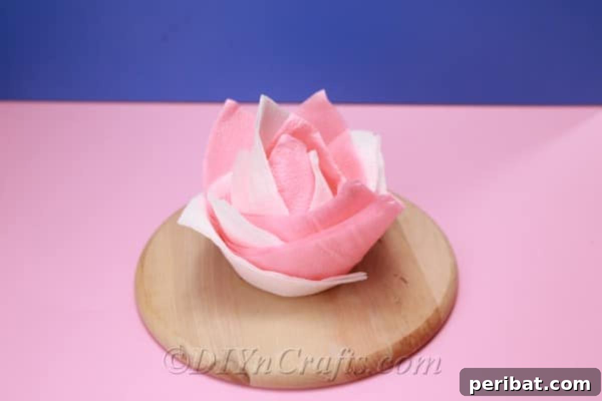 Fold Beautiful Napkin Roses 3 Completed pink and white napkin rose from a napkin folding tutorial, displayed on a wooden board