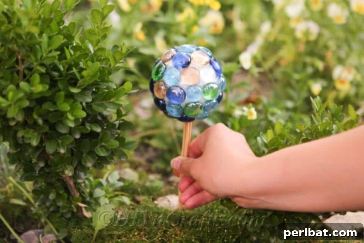Craft Your Own Garden Spheres 4 A hand holds a small, shimmering gazing ball adorned with glass nuggets, surrounded by lush green plants.