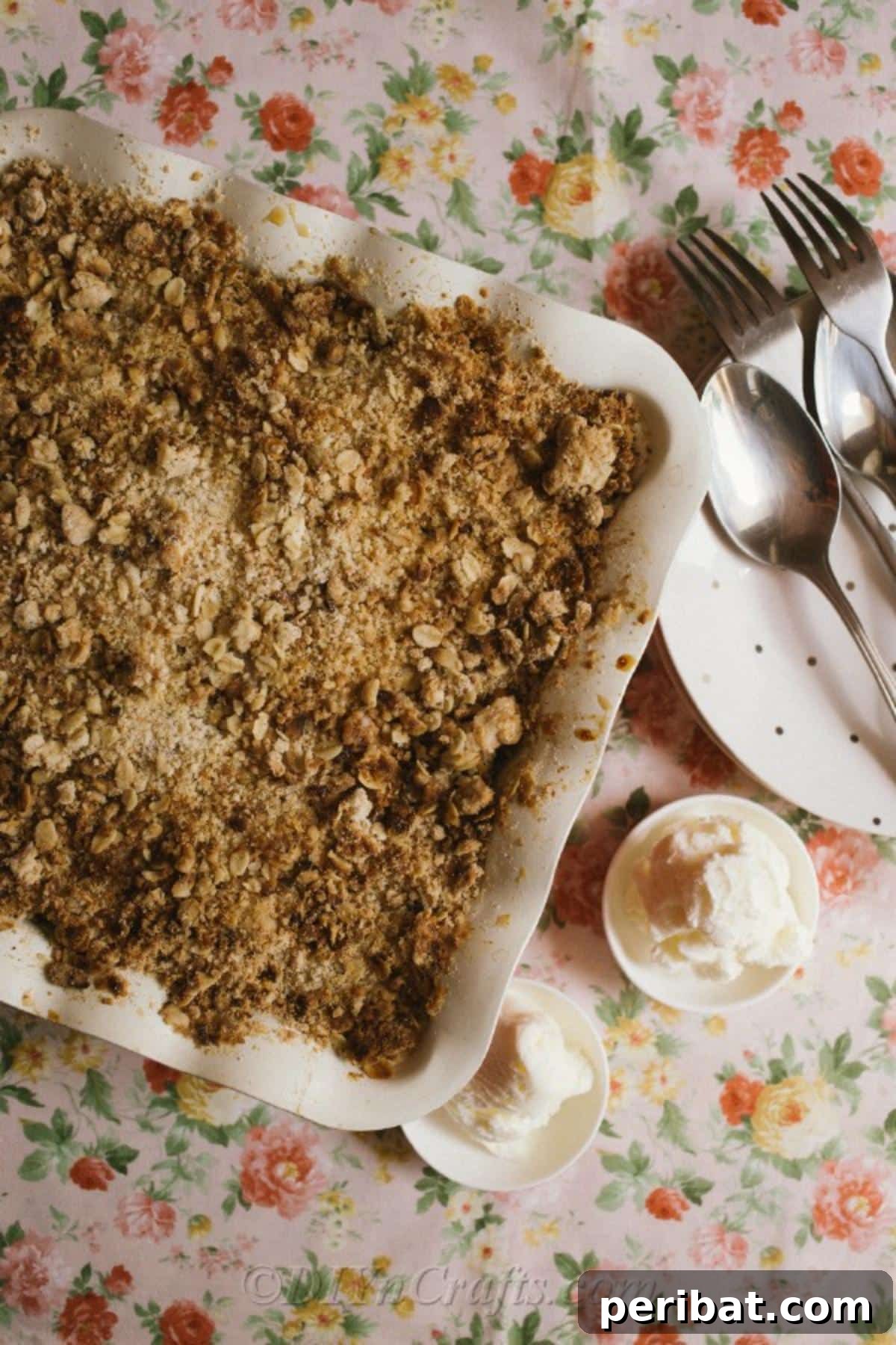 Effortless Homestyle Apple Crumble 7 Overhead picture of a prepared apple crumble recipe in a baking dish sitting on a floral tablecloth next to serving dishes, inviting enjoyment.