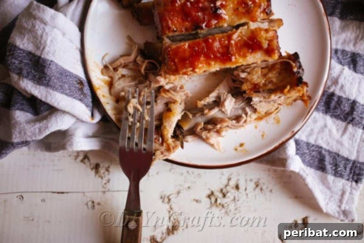 Effortless Fall-Off-The-Bone Oven Ribs 3 Close-up of perfectly seasoned BBQ pork ribs, baked in the oven, resting on a white plate