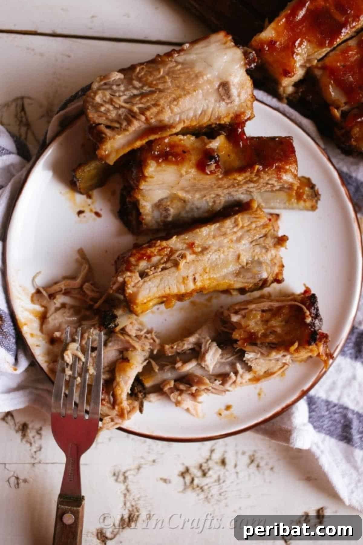 Effortless Fall-Off-The-Bone Oven Ribs 4 Sliced oven baked ribs arranged on a white plate, resting on a white and blue patterned napkin