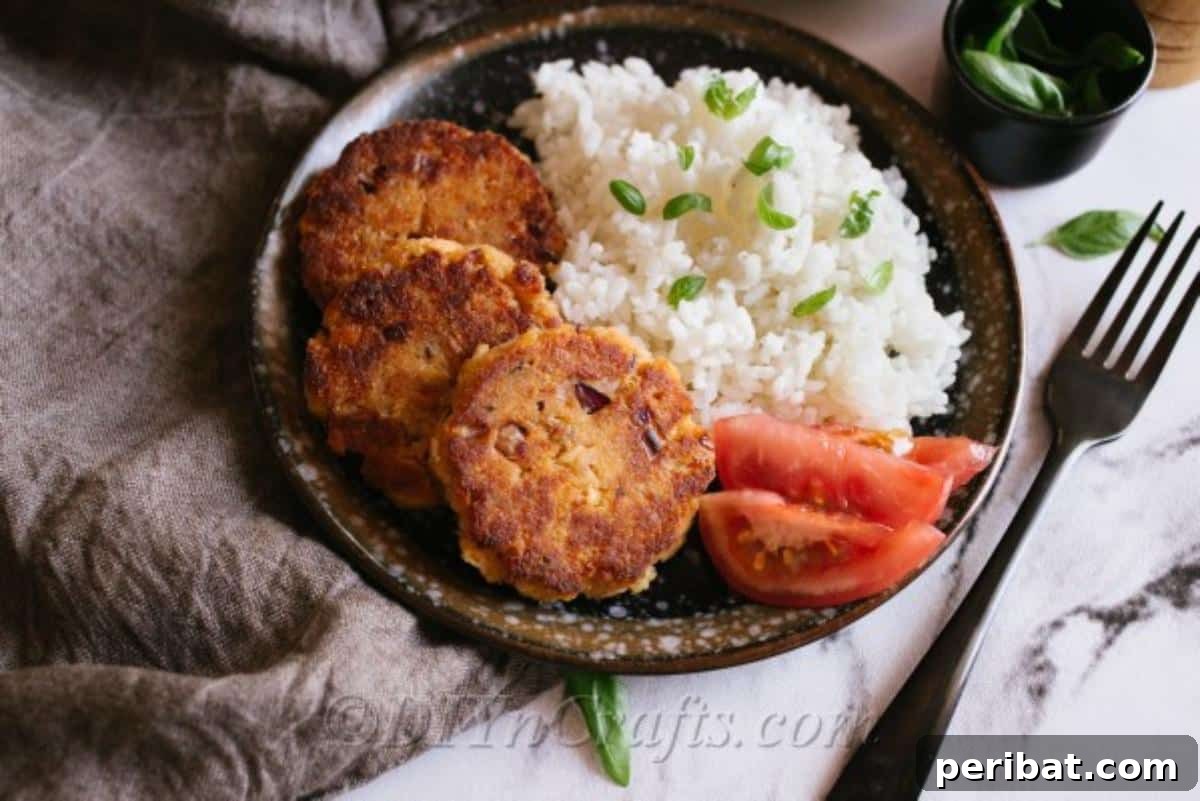A plate of salmon patties with rice and tomato on the side