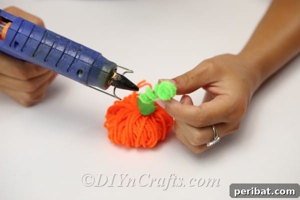 Handmade Autumn Yarn Pumpkin Garland Tutorial 19 A woman hot gluing the leaves and stem to the top of the yarn pumpkin