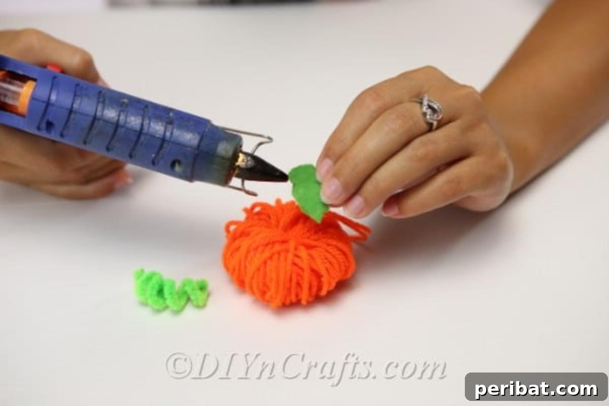 Handmade Autumn Yarn Pumpkin Garland Tutorial 9 Attaching the felt leaf and pipe cleaner stem to the yarn pumpkin for the fall garland craft