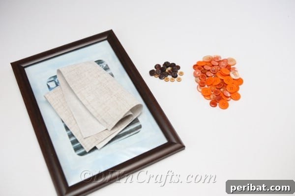 Supplies for pumpkin button art laying on a white table, including various buttons, a frame, and glue