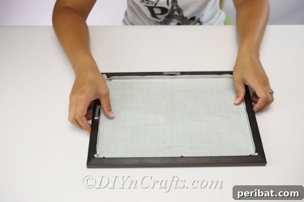 Measuring a piece of fabric against a picture frame to ensure correct sizing for the button art background