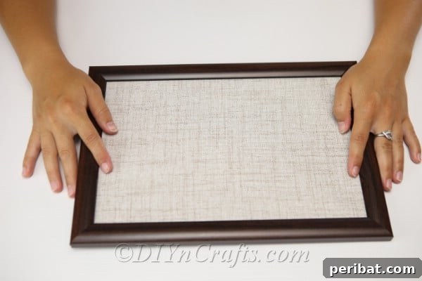 A hand pressing fabric into a picture frame, securing it as the canvas for the button art