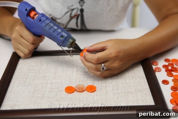 Arranging buttons on the fabric inside a picture frame, starting to form the pumpkin outline for button art