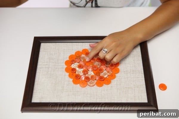 A close-up of a pumpkin shape being filled with various orange buttons on a fabric background for button art