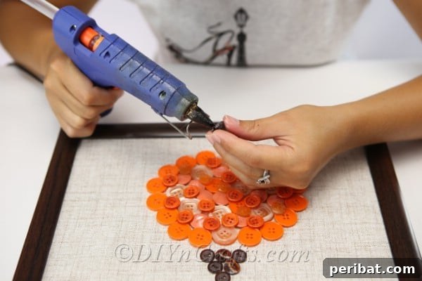 Adding brown buttons to create the stem of the pumpkin, completing the button art design