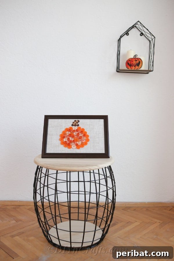 A finished pumpkin button art craft prominently displayed on a wooden and wire stool against a bright white wall