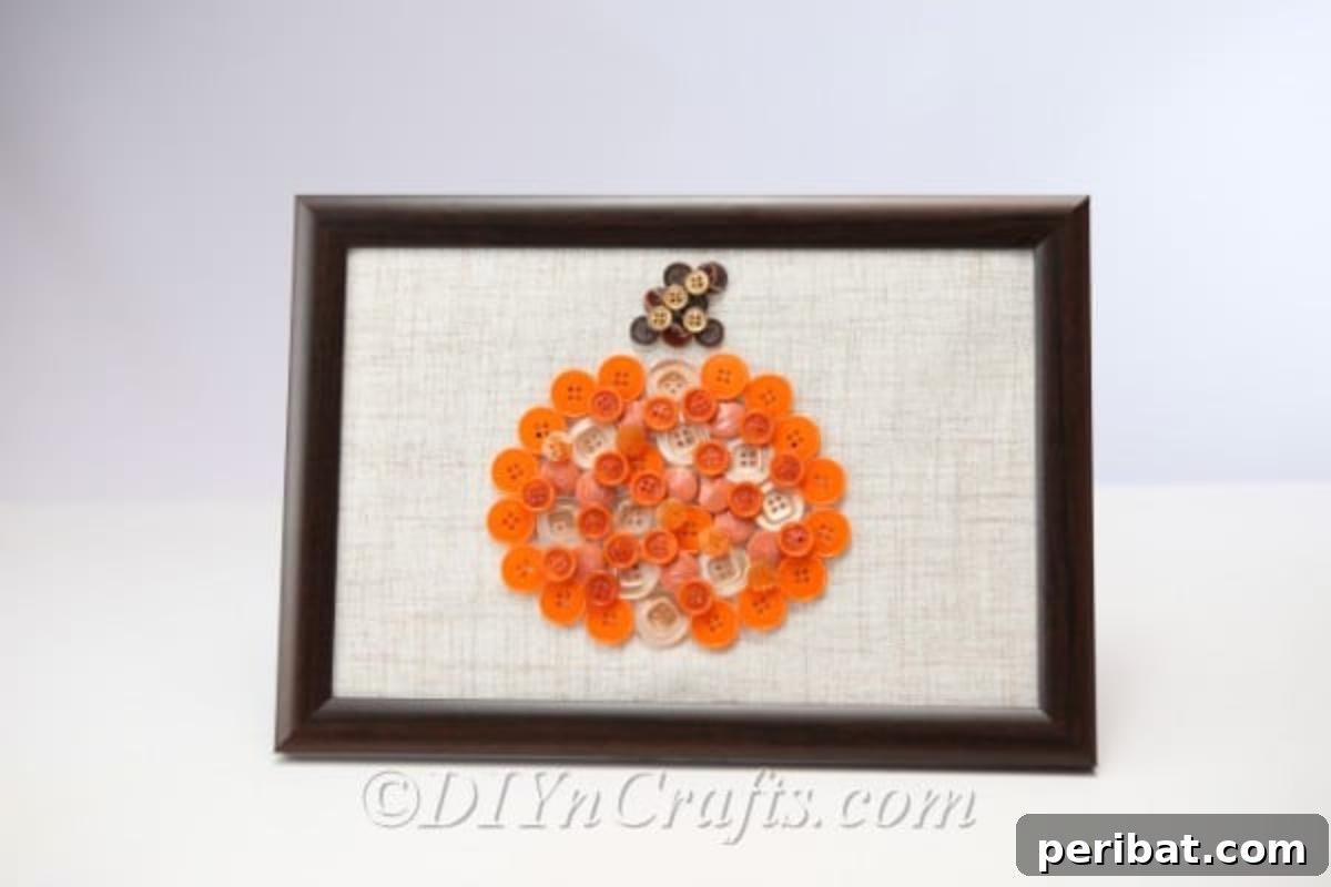 A charming framed pumpkin button art piece displayed on a white wall, highlighting its rustic and handmade appeal