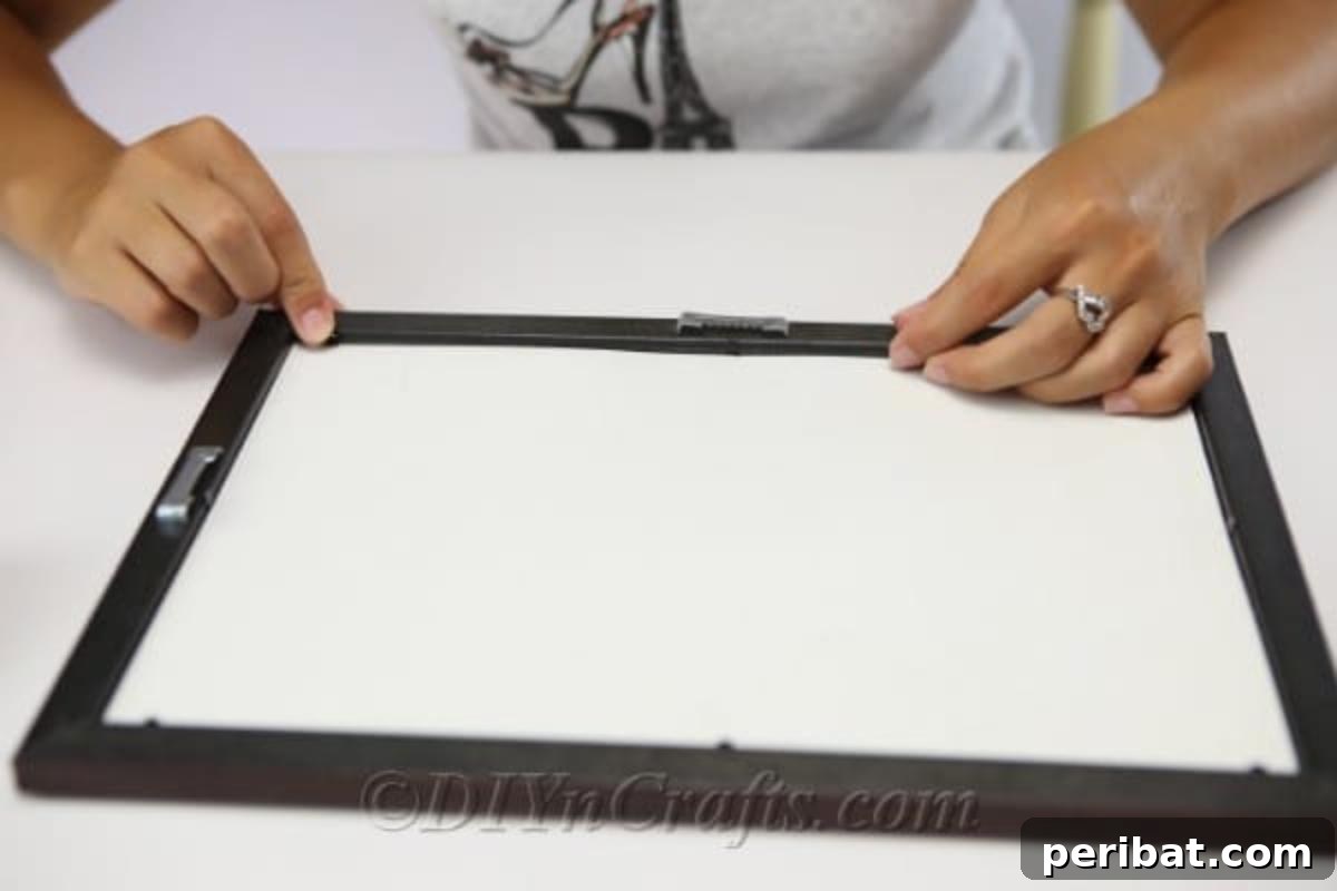 A close-up shot showing the process of removing the back of a picture frame, an initial step in creating button art