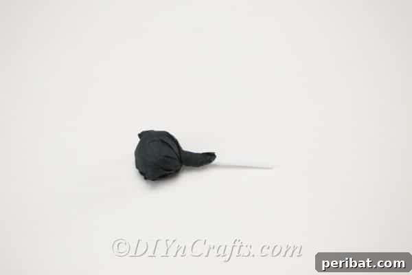 Twisting the tissue paper around the lollipop stick to secure the spider's body.
