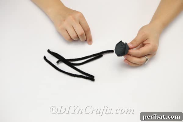 Cutting black pipe cleaners into equal halves to prepare for creating spider legs.
