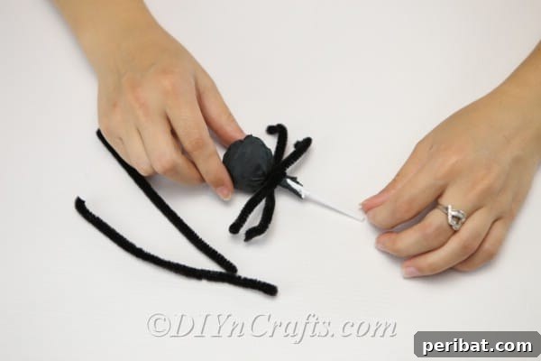 Wrapping pipe cleaner segments around the lollipop stick to form the spider's legs.