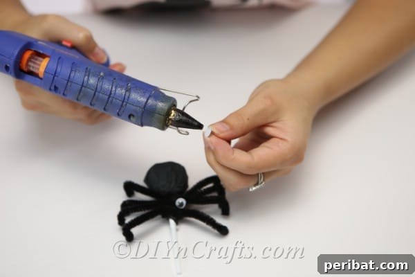 Affixing googly eyes to the front of the spider lollipop to create its face.
