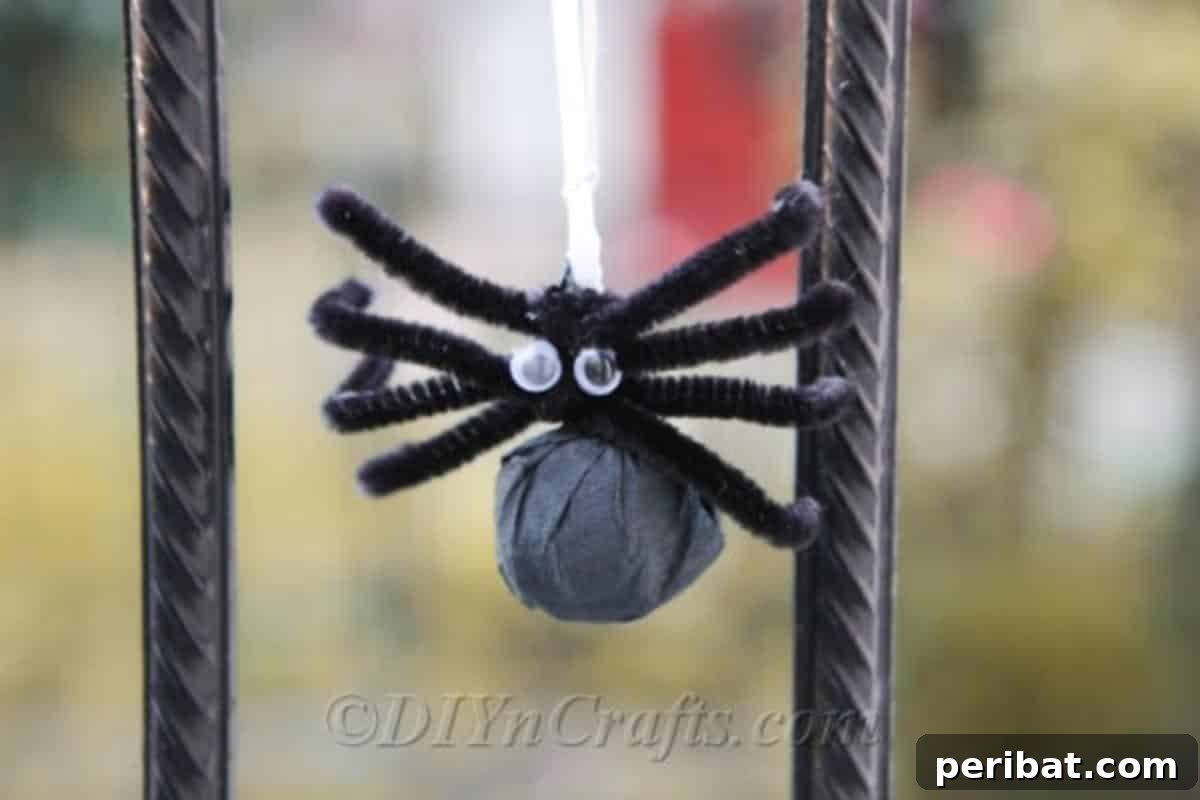 A Halloween lollipop spider craft hanging from a black metal fence outdoors, ready for trick-or-treaters.