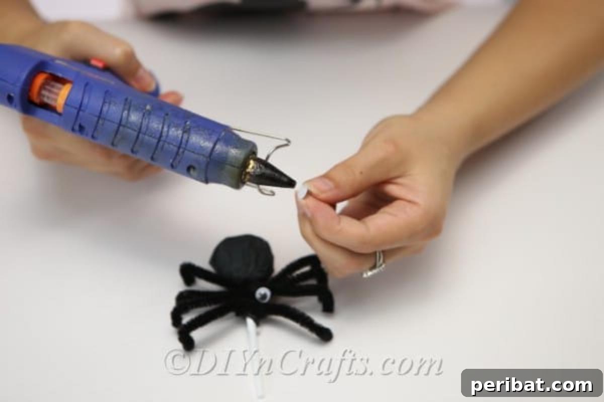Gluing googly eyes onto the black tissue paper-wrapped lollipop, with pipe cleaner legs already attached, to create the spider's face.