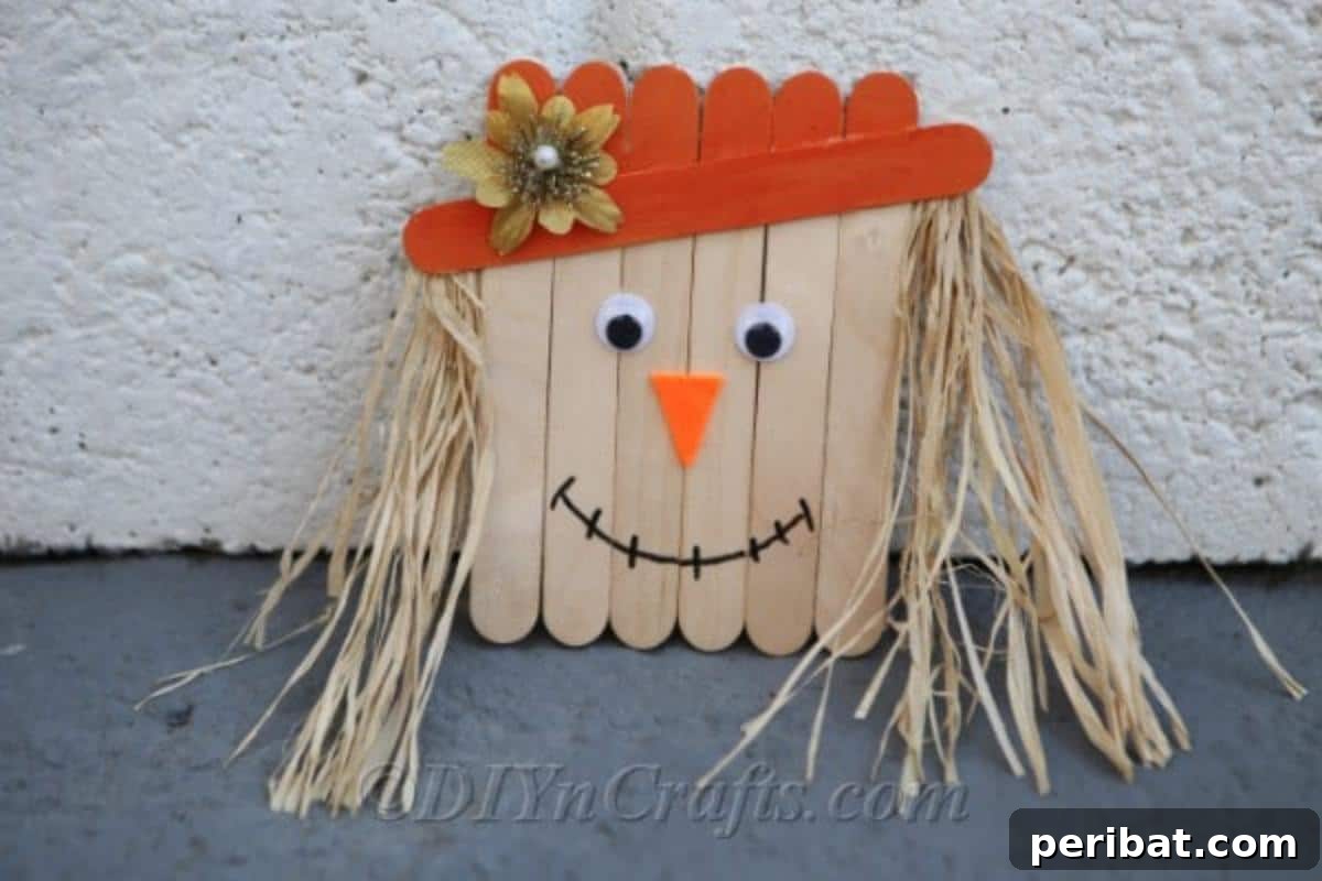 Completed scarecrow from how to make a scarecrow out of craft sticks tutorial sitting against a white wall