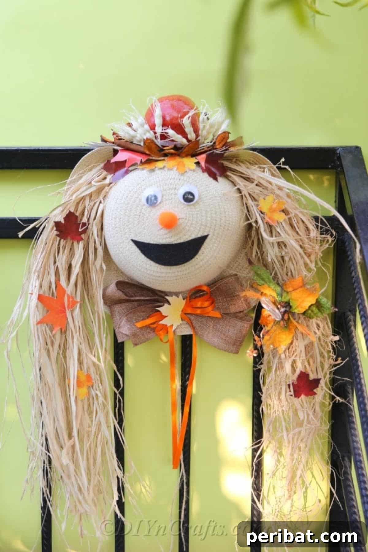 A completed scarecrow harvest decor craft hanging on a metal fence