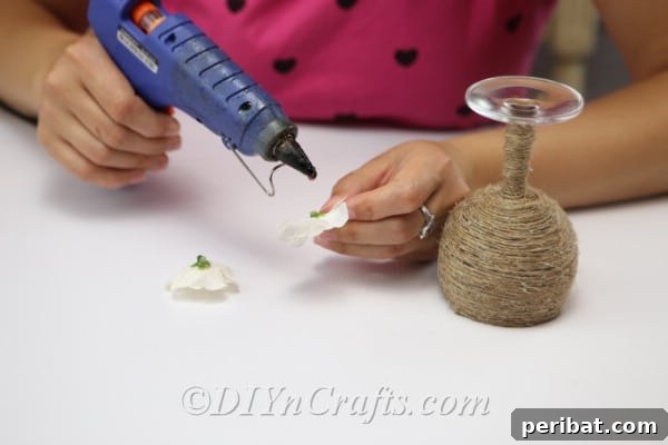 Rustic Glow: DIY Wine Glass Candle Holder 13 Securing faux flowers onto the twine-wrapped wine glass with hot glue for a decorative touch.