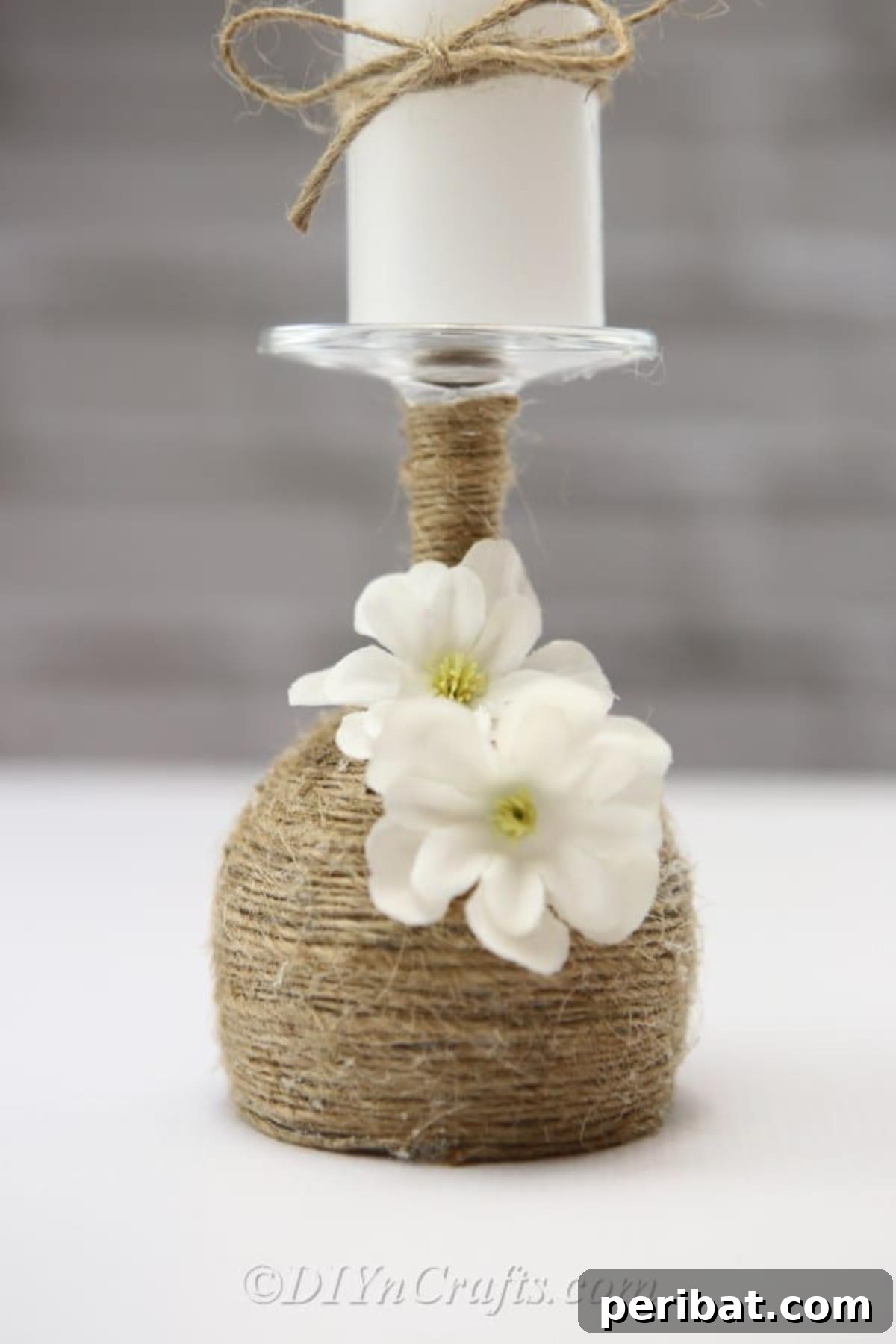 Rustic Glow: DIY Wine Glass Candle Holder 5 A close-up view highlighting the intricate detail of the twine wrapping and the delicately placed faux flowers on the rustic wine glass candle holder.