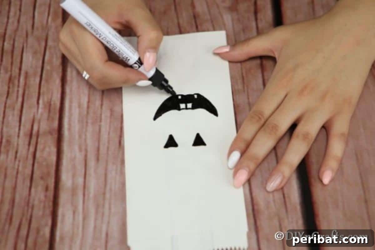 DIY Ghostly Glow Bags for Halloween 7 A smiling face being drawn onto a luminary bag for Halloween, demonstrating the marker technique