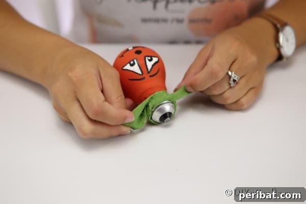 Crafting Spooky Ghosts and Pumpkins from Light Bulbs 17 Tying a green ribbon on the top of a pumpkin decorative light bulb for Halloween