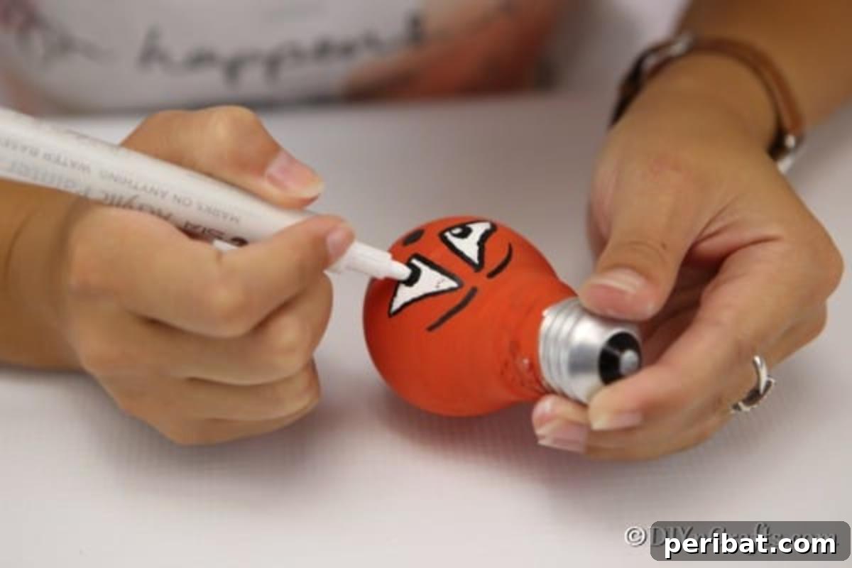 Crafting Spooky Ghosts and Pumpkins from Light Bulbs 8 Drawing face on orange painted decorative light bulb for Halloween
