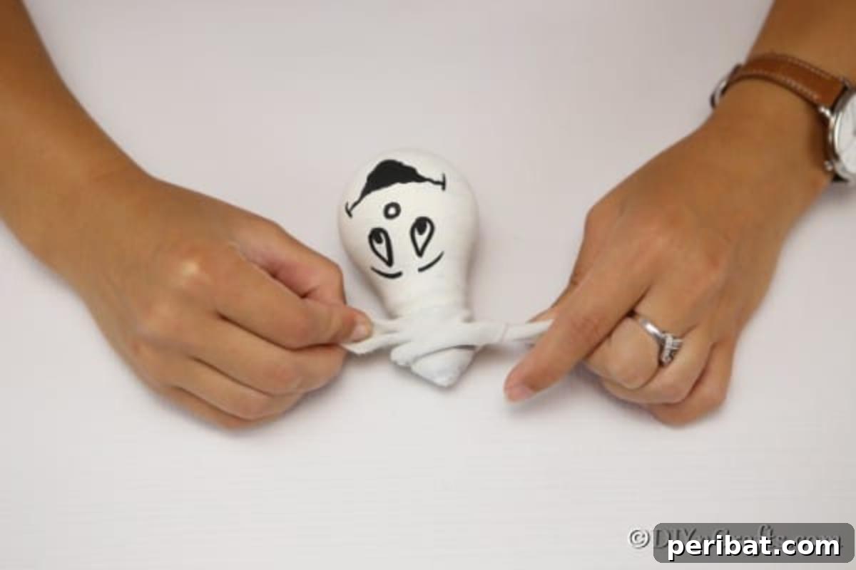 Crafting Spooky Ghosts and Pumpkins from Light Bulbs 9 Tying a ribbon on the ghost decorative light bulbs for hanging