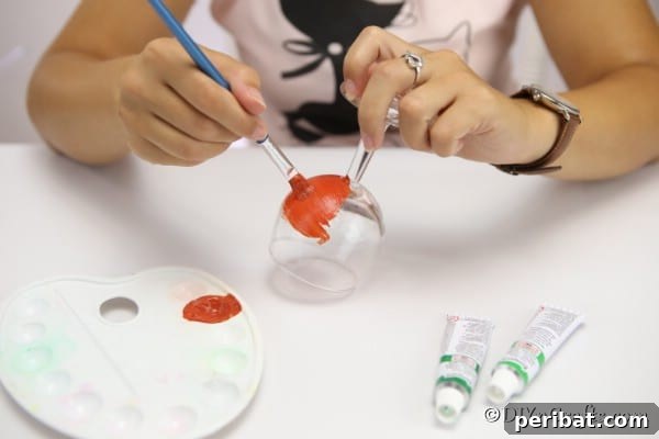 A woman painting the wine glass with orange paint to create a pumpkin