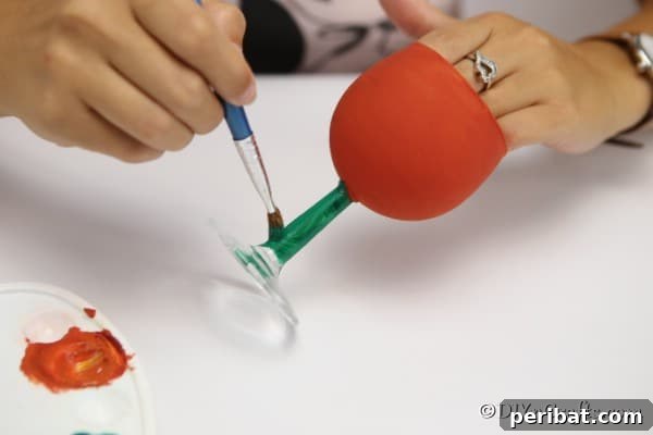 A woman painting the wine glass stem green for the pumpkin art