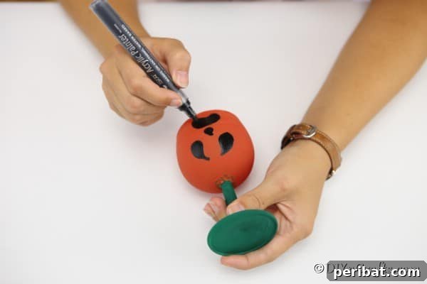 Drawing a face on the dry painted wine glass pumpkin