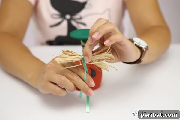 Securing the ribbon and bow to the wine glass pumpkin
