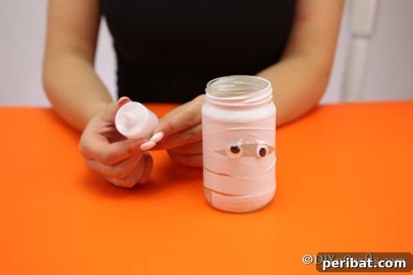The mummy jar, fully wrapped with tape, with the googly eyes peeking through, and a tealight being placed inside.
