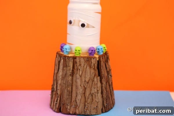 A smaller mummy mason jar light on a wooden block, surrounded by decorative skulls, showcasing its festive appeal.