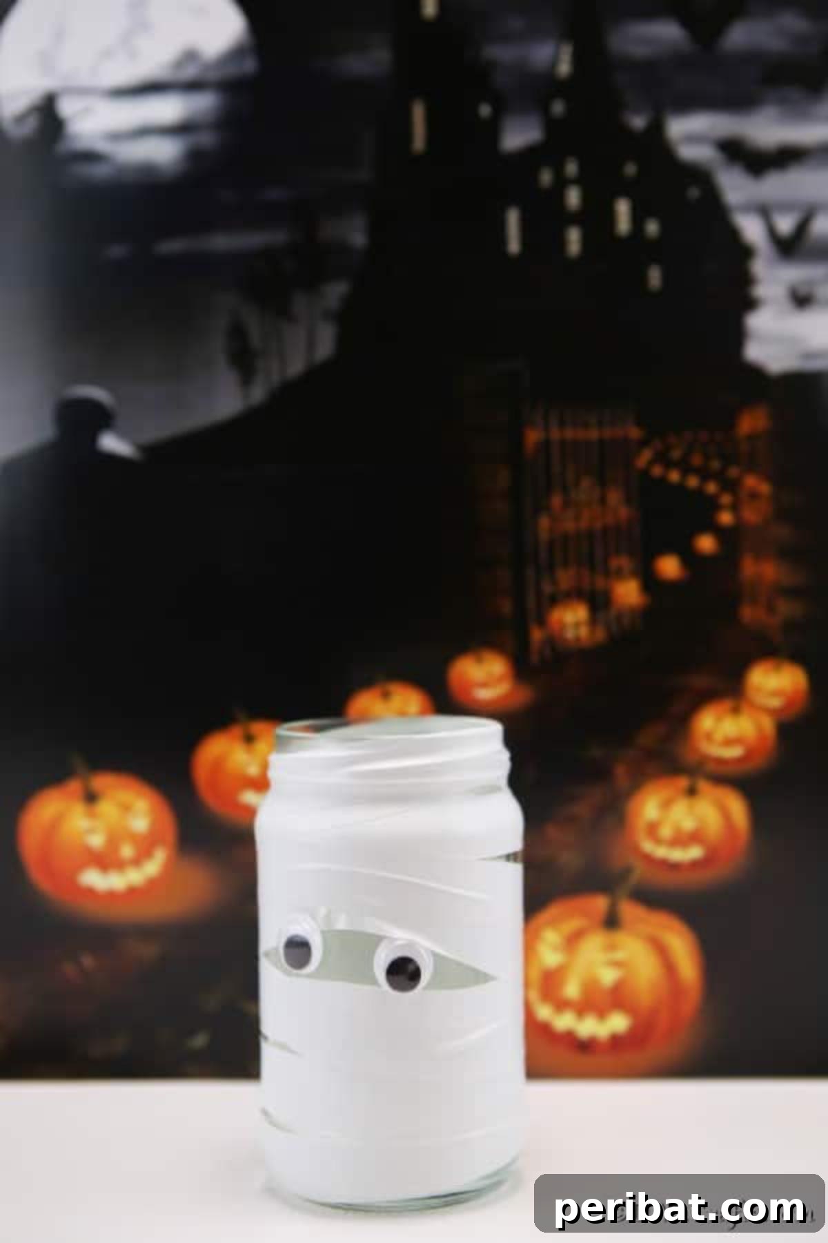 A single mummy mason jar light stands on a white surface with a blurred background of festive Halloween pumpkins, showcasing its unique and simple design.