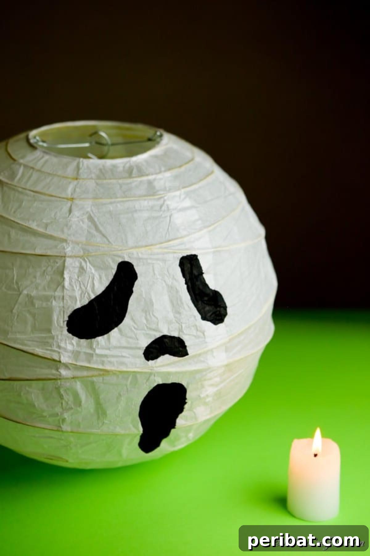 Hauntingly Simple Ghost Lanterns 4 A ghost paper lantern sitting on a green surface next to a battery-operated candle