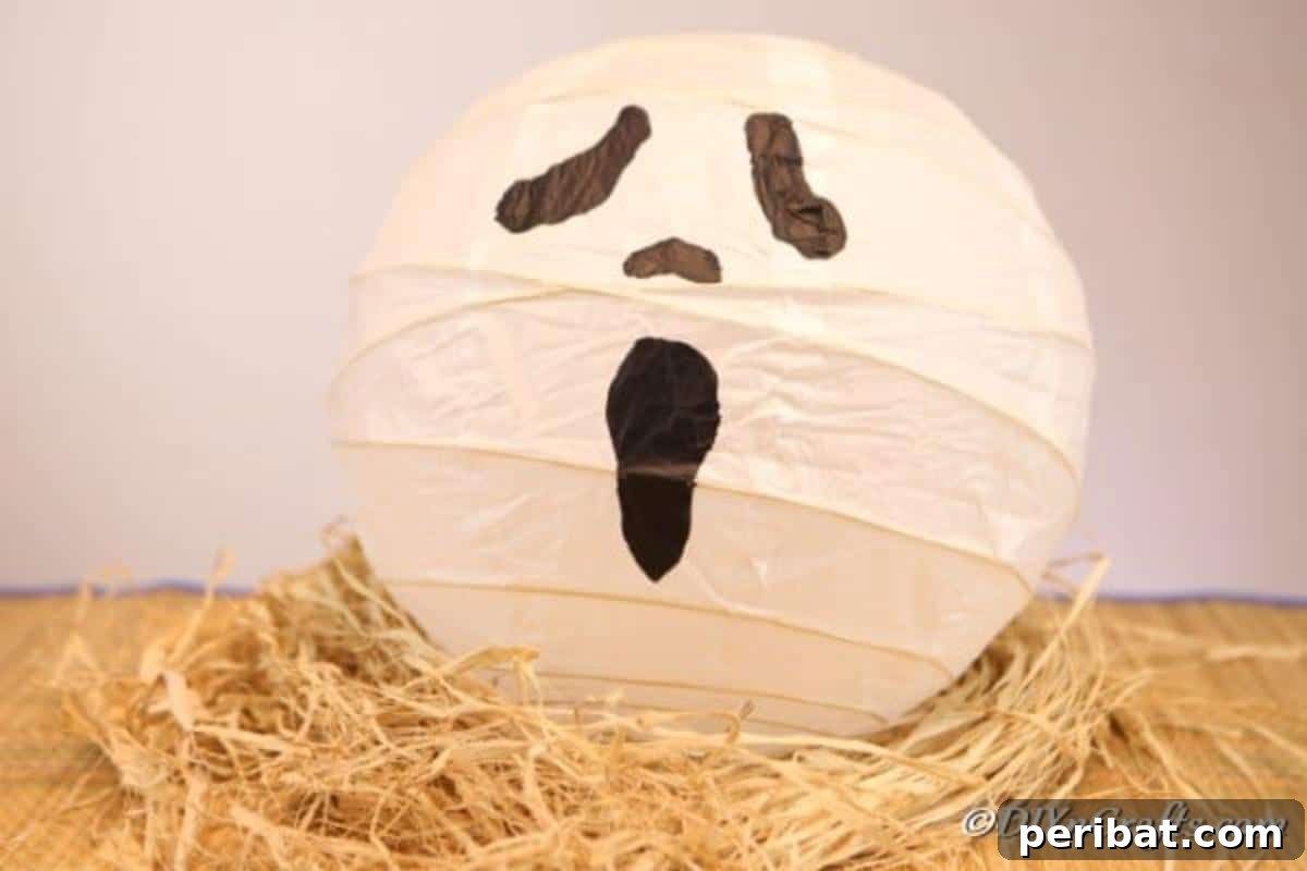 Hauntingly Simple Ghost Lanterns 5 A surprised face ghost paper lanterns craft sitting on a stack of decorative straw