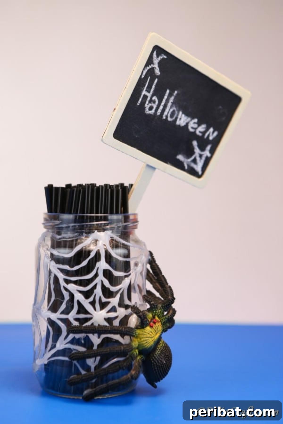 A halloween spider web jar sitting on a blue surface with a halloween sign and knives inside the jar