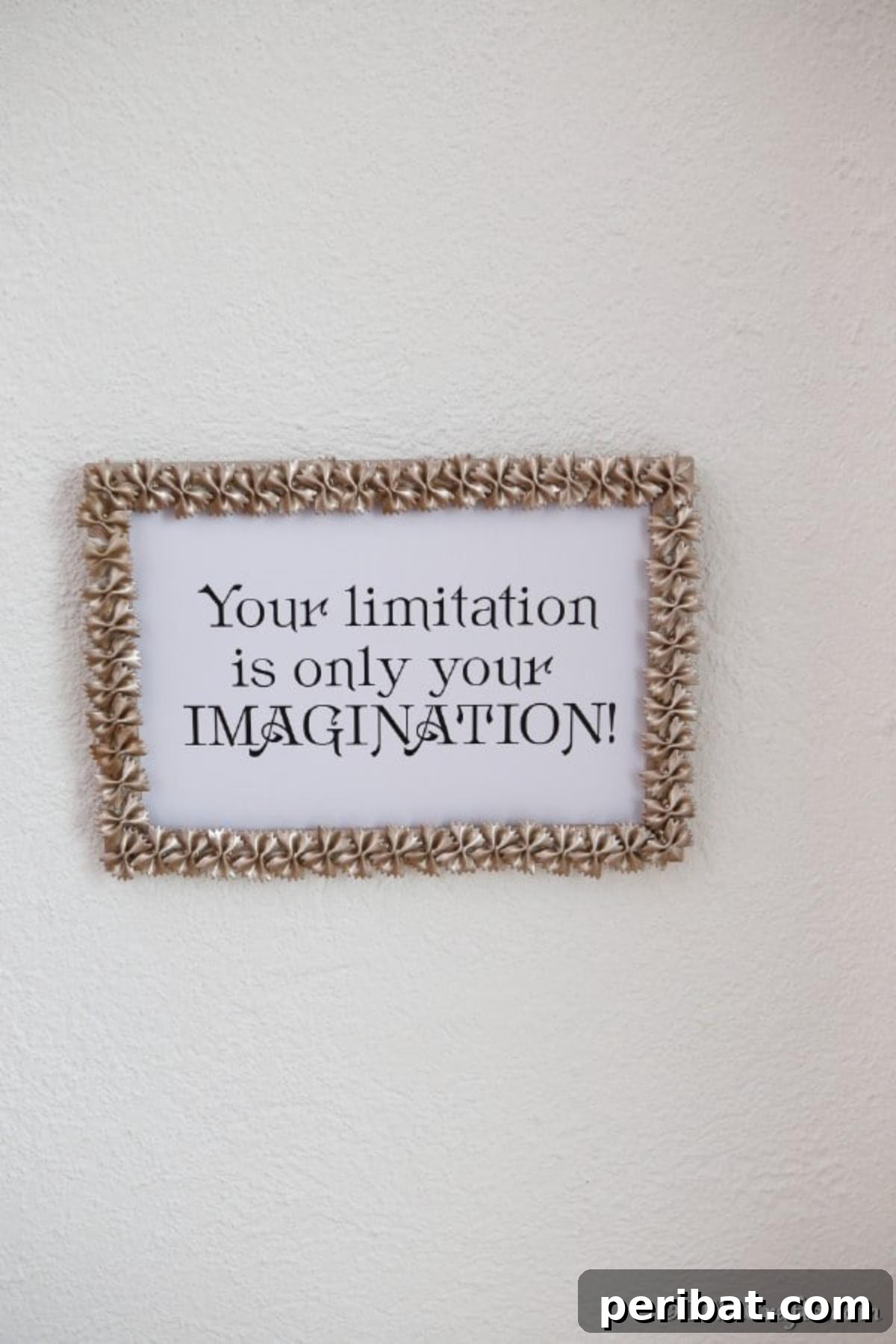 A macaroni art picture frame hanging on a white wall