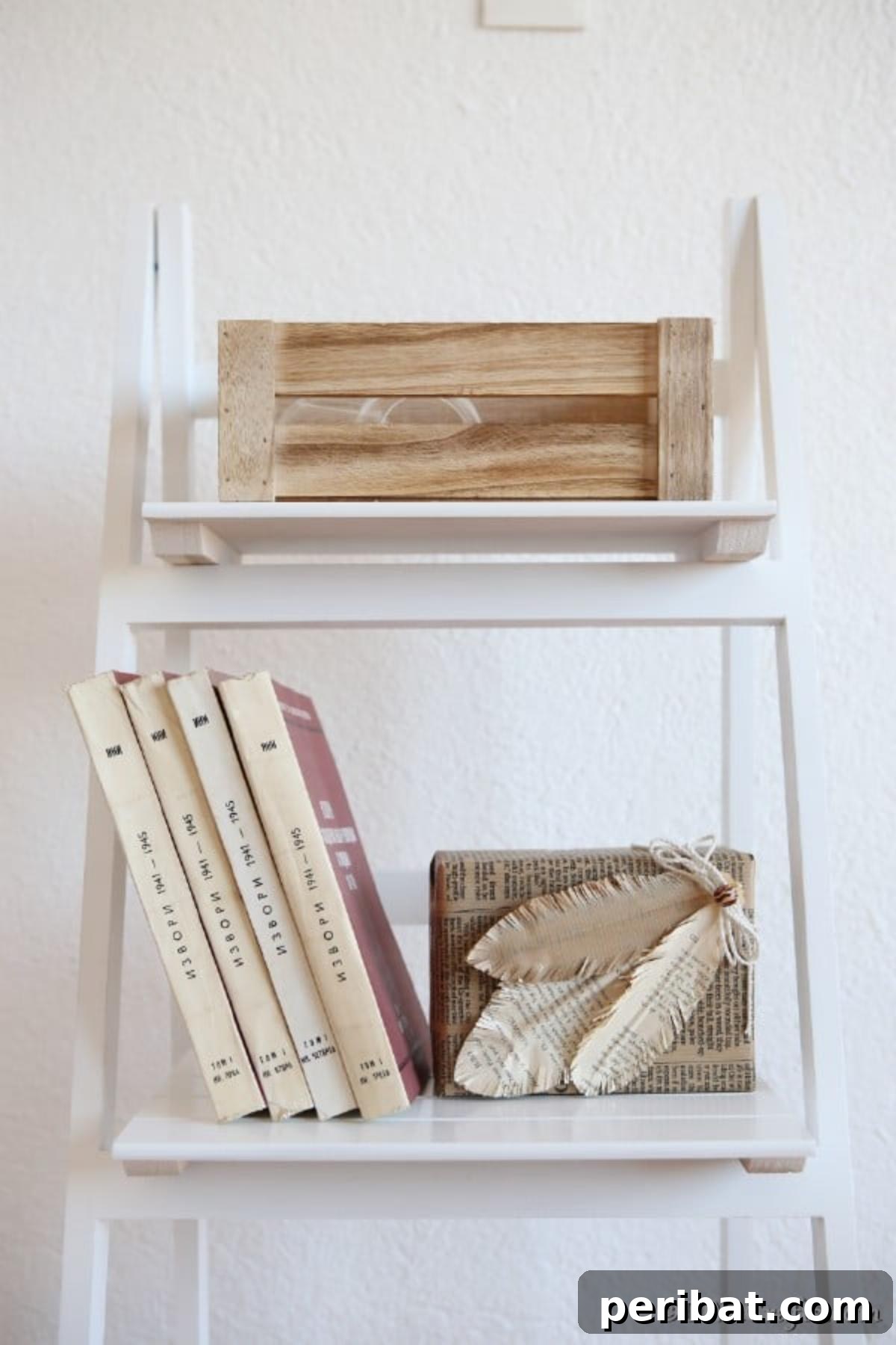 A newsprint-covered box adorned with handmade decorative feathers, displayed on a small white shelf.